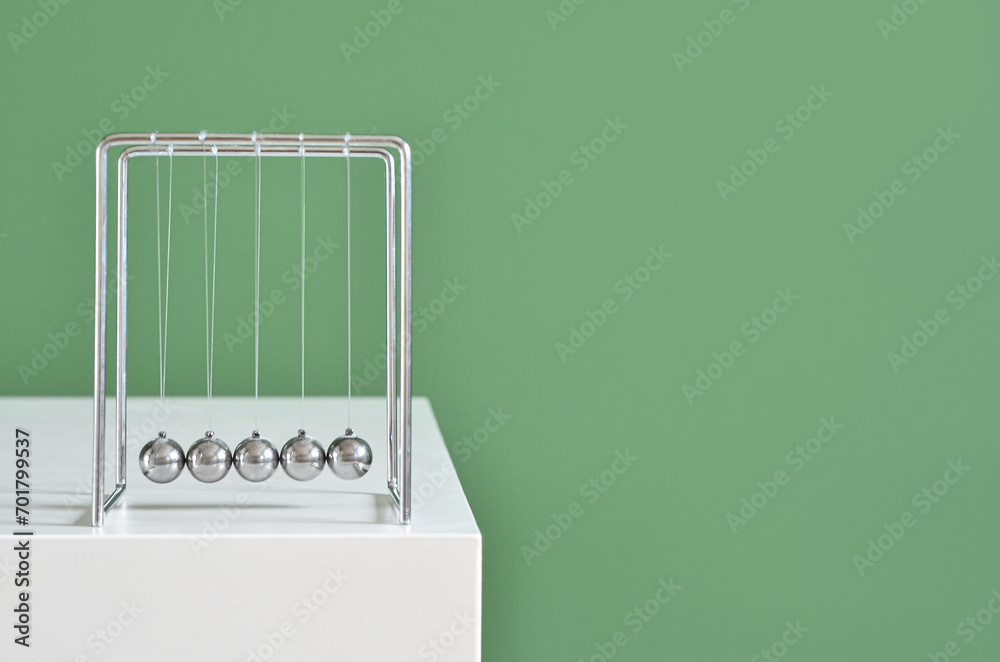 Newton's Cradle on table near green wall