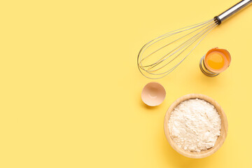 Bowl with wheat flour, cracked egg and whisk on yellow background