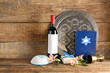 Composition with bottle of wine, Passover Seder plate, cup, Torah, kippah and flowers on wooden background