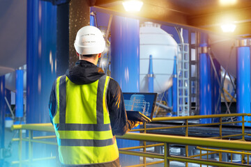 Poster - Man industrial engineer. Guy on territory of plant. Industrialist with laptop with back to camera. Oil refinery engineer. Man stands on industrial mezzanine. Industrial engineer near oil tanks