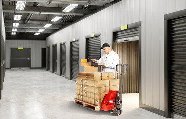 Wall Mural - Man near storage room. Warehouse corridor with pallet jack. Man brought boxes to storage unit. Guy in front gate to warehouse rooms. Storage room rental concept. Warehouse building with black gates