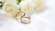 © BlazingDesigns - White flowers and two golden wedding rings on white background.