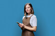 © Valerii Honcharuk - Portrait of young woman in apron holding smartphone in hands on blue background