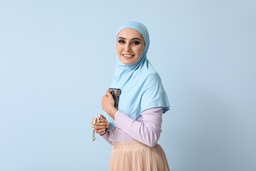 Wall Mural - Young Muslim woman with Koran and prayer beads on blue background. Islamic New Year celebration