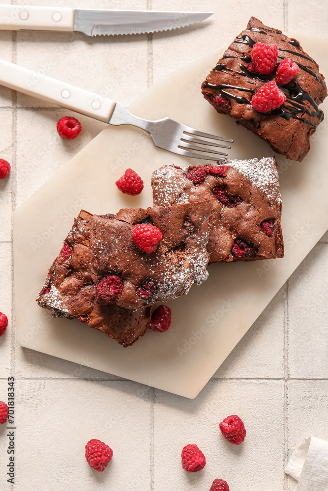 Board with pieces of raspberry chocolate brownie on white tile background