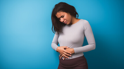 A young woman doubled over in discomfort against a blue backdrop.