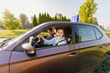 © Iryna - Male instructor satisfied with the ride of his female student, he comments on her correct actions inside car. Two people are riding in a brown car with blue L plate on a roof.