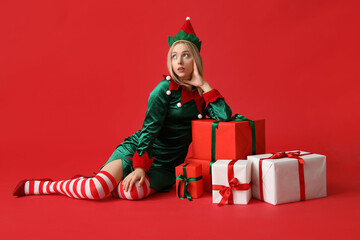 Wall Mural - Young woman in elf costume with Christmas gift boxes on red background