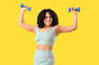 Sporty adult woman with dumbbells on yellow background