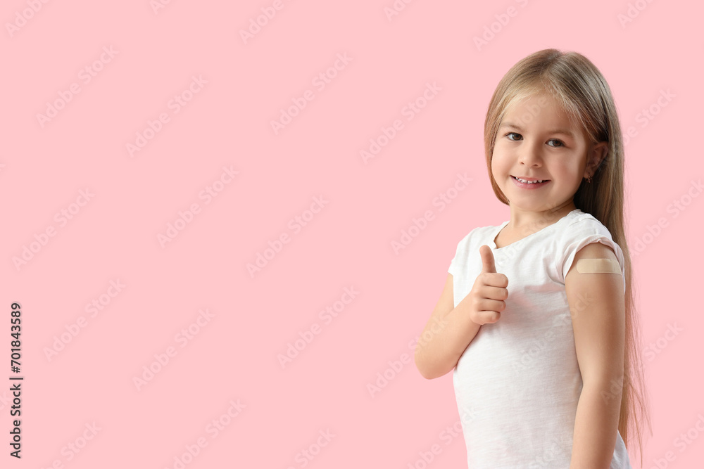 Little girl with patch showing thumb-up after vaccination on pink background