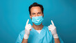 Male healthcare professional with dark hair in a white lab coat wearing a surgical mask and blue latex gloves, poised in a sterile environment
