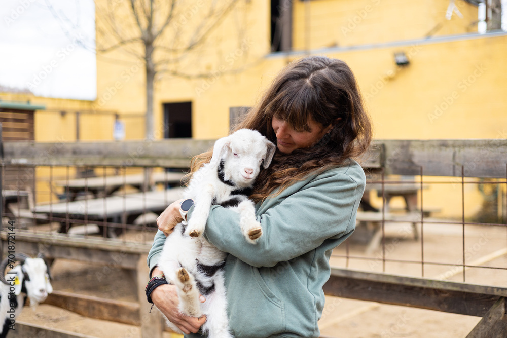 Happy young farmer woman hugging a baby goat on a rural organic farm ...