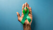 Green ribbon on blue background. Cancer Awareness Month. Copy space.