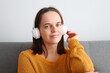 © sementsova321 - Beautiful attractive cute relaxed woman listening to music with headphones sitting on sofa at home enjoying favorite playlist looking at camera with smile