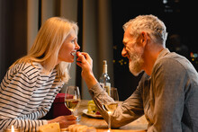Loving Mature Husband Treating His Wife With A Grape During Romantic Dinner