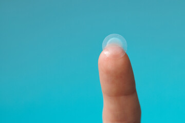 close-up round acne patch on finger on blue background. acne patches for treatment of pimple and ros