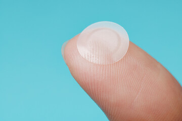 close-up round acne patch on finger on blue background. acne patches for treatment of pimple and ros