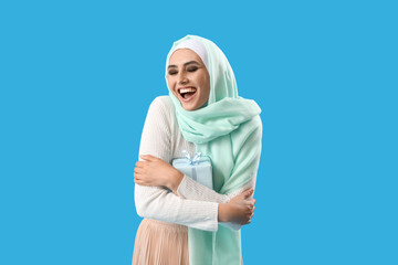 Wall Mural - Young Muslim woman with gift on blue background. Islamic New Year celebration