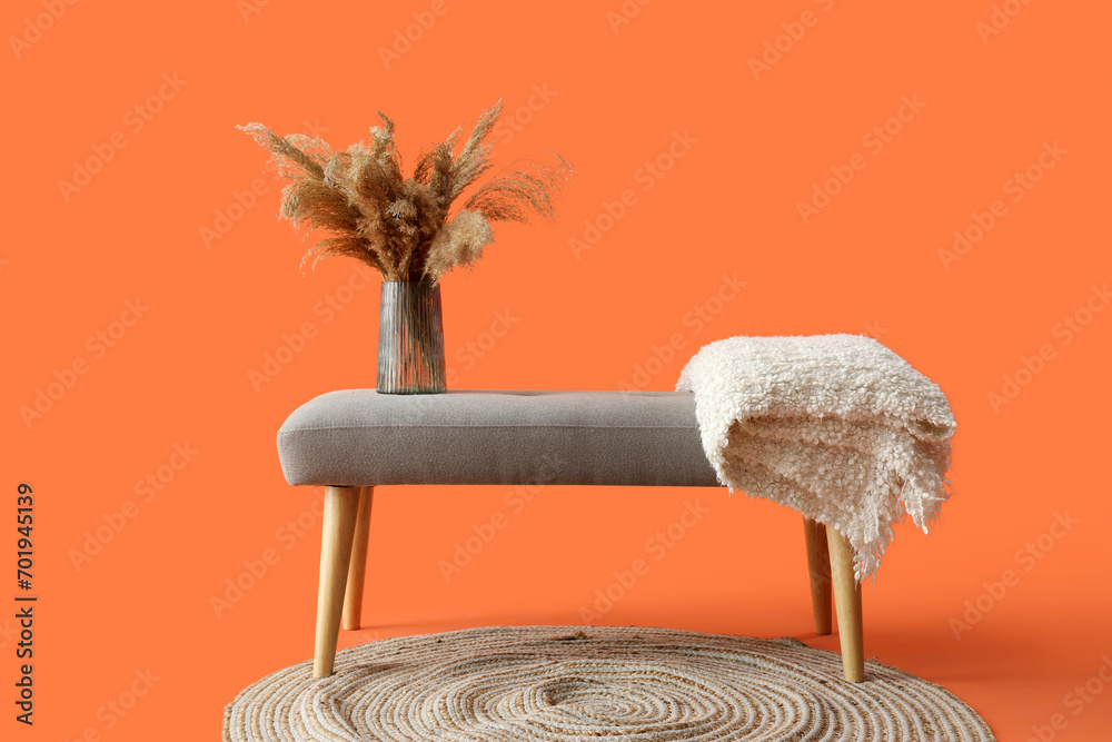 Vase with pampas grass on soft bench against orange background