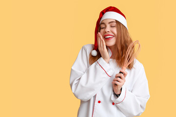 Poster - Portrait of pleased female chef in Santa hat with whisk on yellow background