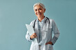 © HBS - Family doctor. A female employee of a medical clinic poses on a blue background.