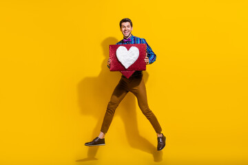 Poster - Full size photo of cheerful guy dressed striped shirt jumping with big social media like box in arms isolated on yellow color background