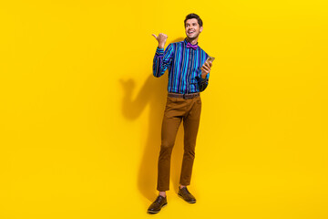Poster - Full body photo of optimistic man wear bow tie hold smartphone look directing at offer empty space isolated on yellow color background