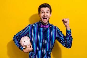 Poster - Photo of overjoyed guy with stubble dressed striped shirt hold monye box raising fist up win bet isolated on yellow color background