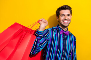 Poster - Portrait of toothy beaming guy dressed stylish shirt bow tie hold shopping bags buy new clothes isolated on bright yellow color background