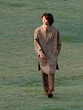 Portrait of a handsome Chinese young man in khaki overcoat with hand in pocket walking on green grass field in sunny day, male fashion, cool Asian young man lifestyle.
