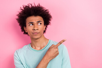 Poster - Photo of doubtful unsure man dressed blue t-shirt pointing finger looking empty space isolated pink color background