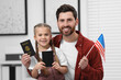 © New Africa - Immigration. Happy man with his daughter holding passports and American flag indoors