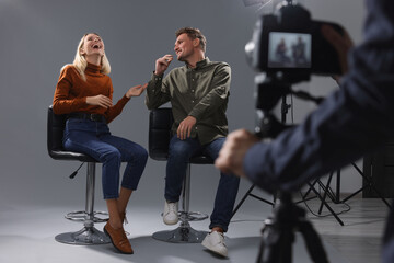 Poster - Casting call. Man and woman performing while camera operator filming them against grey background in studio