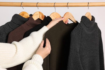 Wall Mural - Woman taking sweater from rack on light background, closeup