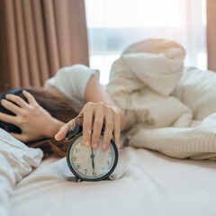 Wall Mural - alarm clock and asian woman hand stop time in bed while sleeping, young adult female wake up late in the early morning. Relaxing , sleepy, daily routine and have a nice day concepts