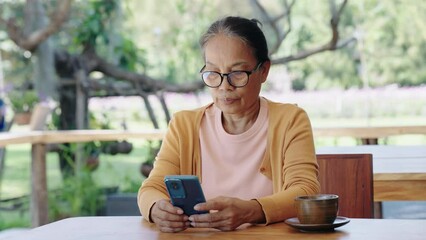 Senior woman using mobile phone touching scroll page app on mobile phone at room.Manager typing telephone alone watch film online.