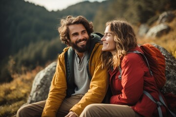 Wall Mural - Happy young couple sitting on top of a mountain and looking at each other, Carefree couple enjoys in view while taking break during hiking in nature, AI Generated