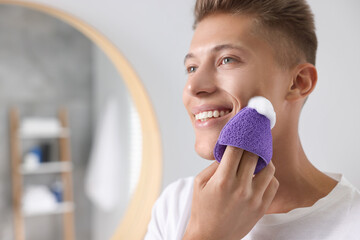 Sticker - Happy young man washing his face with sponge in bathroom. Space for text