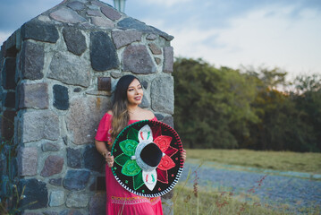 Wall Mural - Mexican woman wearing traditional hat and dress. Outdoor portrait next to stone wall.