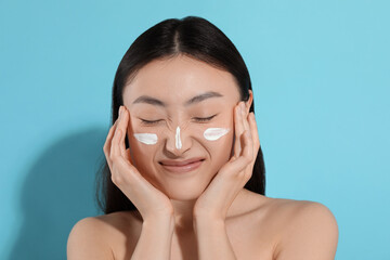 Poster - Beautiful young woman with sun protection cream on her face against light blue background