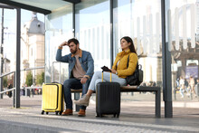 Being Late. Worried Couple With Suitcases Sitting At Bus Station Outdoors