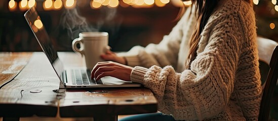 Poster - Female person sitting at wooden table and holding cup of hot drink while surfing the internet on notebook. with copy space image. Place for adding text or design