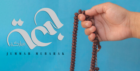 Jummah Mubarak blessed happy Friday Arabic calligraphy, Selective focus image hand of Muslim woman holding prayer beads.