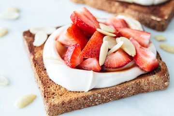 Canvas Print - Crispy breakfast toast with ricotta, strawberries and almonds on white marble background.