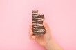 Baby girl hand holding and showing bitten bar with dark brown chocolate glaze and white stripes on light pink table background. Pastel color. Sweet snack. Closeup. Top down view.