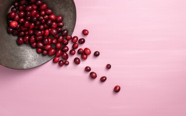 Wall Mural - Fresh, ripe, red cranberries spilling out of an antique colander onto a pink background.