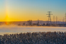 Powerful Power Lines Stretching Across A Foggy River. Mysterious Winter Fog Creates An Unearthly Atmosphere. The Calm Of The Early Morning Is Disturbed By The Hum Of Electricity.