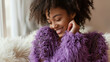 © Leopoldine - Photographie de mode d'une jeune femme métis heureuse de porter un pull en laine mohair à grosses mailles duveteuse de couleur violet, fond clair d'un intérieur cosy et cocooning
