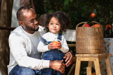 Happy multiracial family having fun camping together. Portrait of multiethnic father and little biracial daughter playing with apple relaxing at backyard. Diverse ethnic dad bonding with cheerful kid.