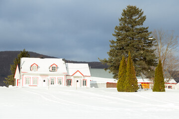 Wall Mural - Beautiful patrimonial double wooden white house with shingled pitched roof and wooden barns seen during a cloudy day after a fresh snowfall, Quebec City, Quebec, Canada